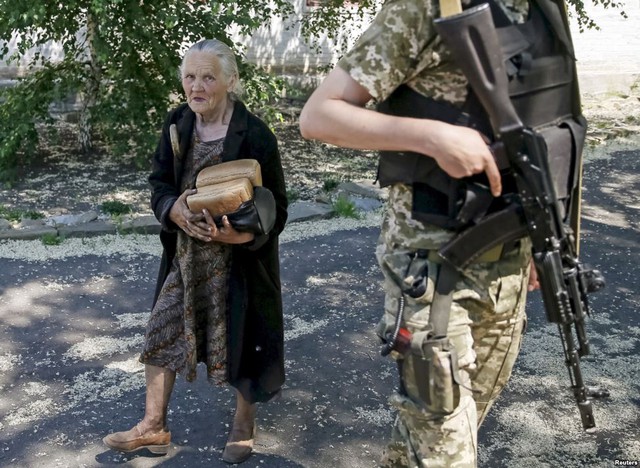 Người dân địa phương mang bánh mì đi qua một binh sĩ Ukraine đứng gác tại ngôi làng Novotoshkivske gần chiến tuyến với phe ly khai thân Nga ở miền đông Ukraine.