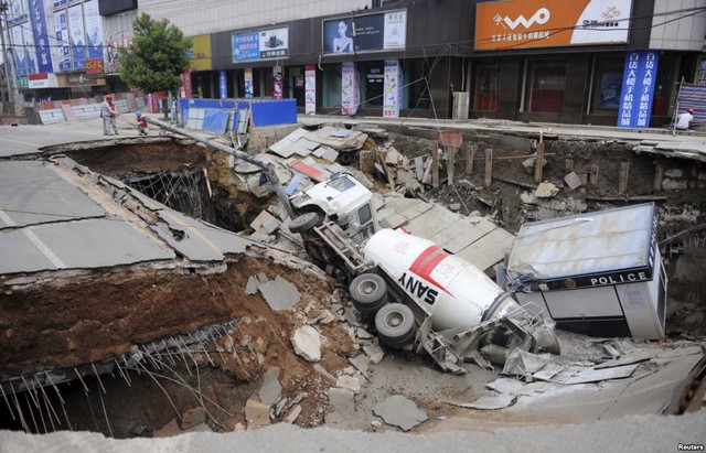 Các công nhân đứng cạnh xe trộn bê tông và đồn cảnh sát di động rơi xuống hố sâu trên đường phố ở tỉnh An Huy, Trung Quốc.