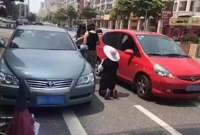 Chiếc xe màu đỏ va chạm với xe ba gác và người phụ nữ trung niên đang quỳ dưới đất để xin bớt tiền bồi thường.