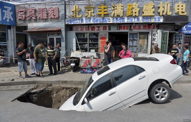 Người qua đường nhìn chiếc ô tô bị rơi một phần xuống hố tử thần xuất hiện trên phố ở Bắc Kinh, Trung Quốc.
