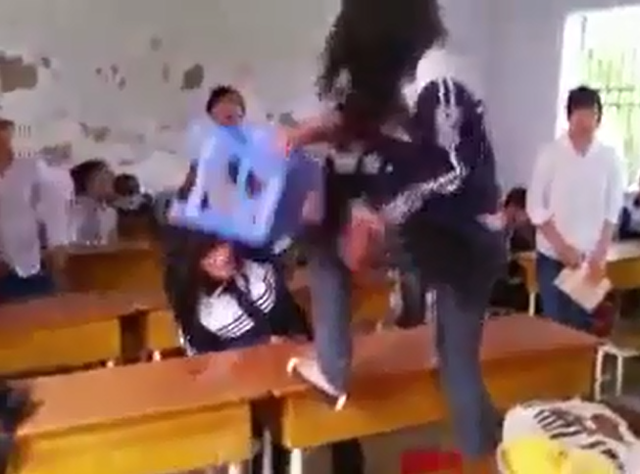 
Cô gái hung hăng cầm ghế, trèo lên bàn rồi đập liên tục vào người bạn học (Ảnh cắt từ clip).
