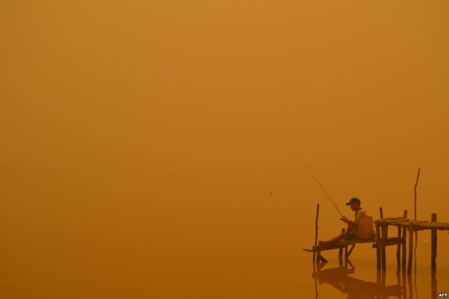 Người đàn ông ngồi câu cá trên bờ sông dười màn sương khói dày đặc ở thành phố Palangkaraya, Indonesia.
