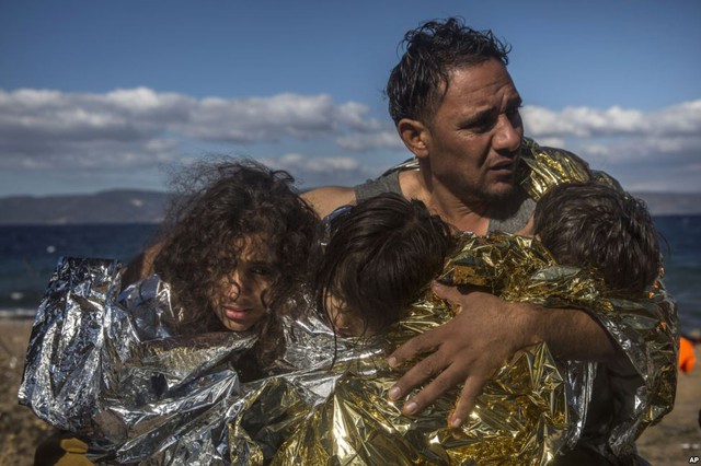 Người đàn ông di cư ôm ba đứa con nhỏ được quàng chăn nhiệt sau khi họ vượt biển từ Thổ Nhĩ Kỳ tới đảo Lesbos, Hi Lạp.