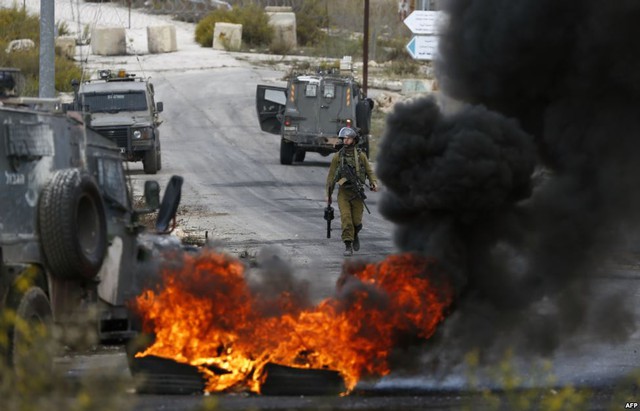 Thành viên của lực lượng an ninh Israel bước đi sau những chiếc lốp xe cháy trong cuộc đụng độ với người biểu tình Palestine ở ngoại ô thành phố Ramallah, Bờ Tây.