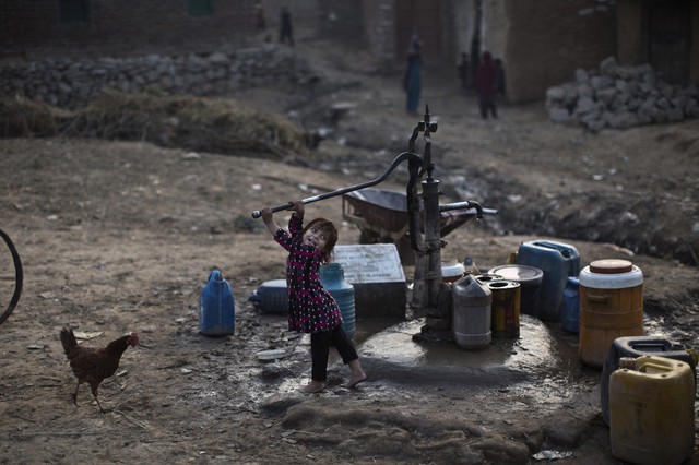 Một em bé tị nạn Afghanistan bơm nước từ giếng khi chờ đợi chị gái trong một khu ổ chuột ở ngoại ô Islamabad, Pakistan.