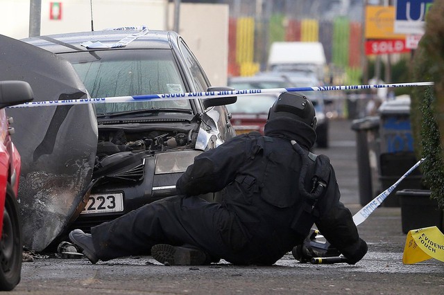 Một sĩ quan kỹ thuật của quân đội Anh kiểm tra chiếc xe bị phá hủy bởi một quả bom ở Tây Belfast, Bắc Ireland.