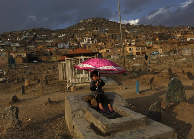 Bé gái cầm ô ngồi trên ngôi mộ tại một nghĩa trang ở thành phố Kabul, Afghanistan.