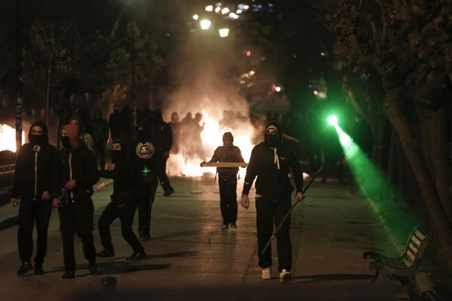 Những thành niên bịt mặt ném đá và chiếu laser vào cảnh sát chống bạo động trong cuộc đụng độ ở Athens, Hi Lạp.