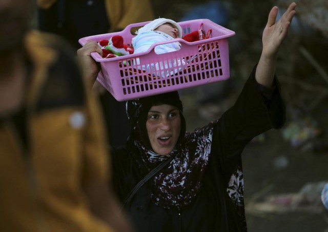 Một phụ nữ đội con nhỏ trên đầu trong khi chạy khỏi khu vục xung đột ở thành phố Ramadi, Iraq.