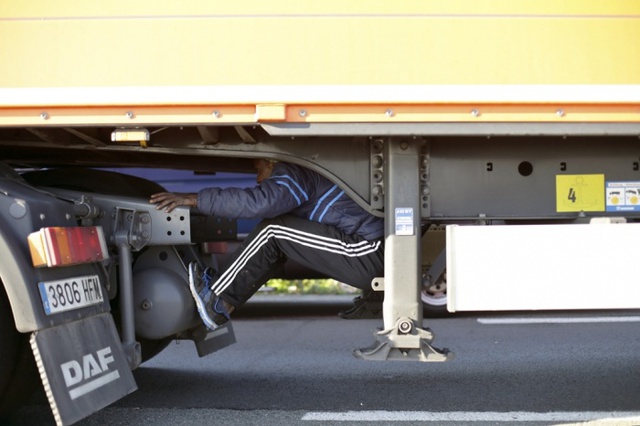 Một người nhập cư trái phép trốn dưới xe tải ở Calais, Pháp, để sang nước Anh.
