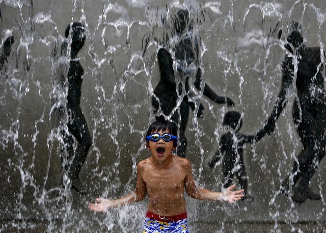 Cậu bé thích thú tắm mát trong đài phun nước trong một ngày nắng nóng ở Tokyo, Nhật Bản.