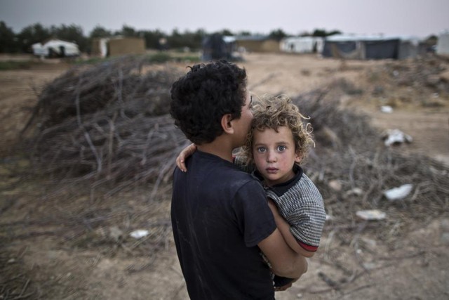 Cậu bé tị nạn người Syria bế em trai trở vệ túp lều của họ tại khu định cư tạm ở ngoại ô Mafraq, Jordan.