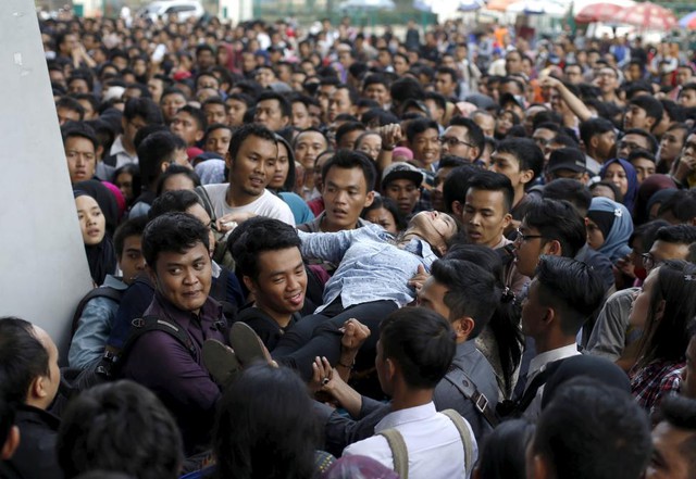 Mọi người đưa một phụ nữ bị ngất xỉu ra ngoài tại hội chợ việc làm với hàng nghìn tham dự ở Jakarta, Indonesia.