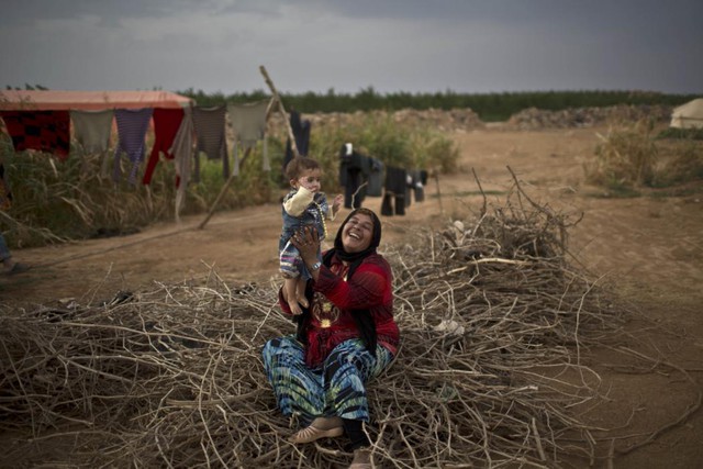 
Người tị nạn Syria chơi đùa với con gái nhỏ trên đống củi khô ngoài lều của họ tại trại tị nạn ở ngoại ô thành phố Mafraq, Jordan.
