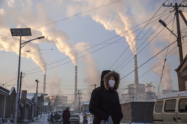 Người phụ nữ đi gần một nhà máy nhiệt điện chạy bằng than xả khói nghi ngút tại tỉnh Sơn Tây, Trung Quốc.