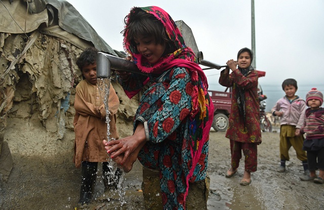 Bé gái tị nạn rửa chân tại một vòi bơm nước trong khi chờ đợi cha mẹ đi lấy thực phẩm cứu trợ từ Chương trình Lương thực Thế giới tại Kabul, Afghanistan.