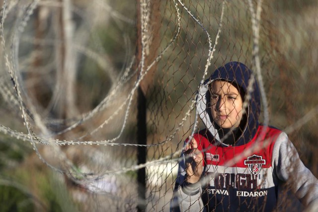 Cậu bé người Palestine đứng sau hàng rào để chờ giấy phép qua cửa khẩu Rafah sang Ai Cập.