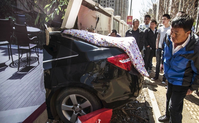 Người qua đường kiểm tra một chiếc ô tô đâm xuyên tường của một công trường xây dựng ở thành phố Thẩm Dương, Trung Quốc.