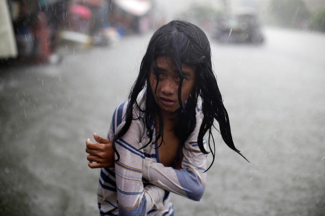 Bé gái cố gắng giữa ấm cơ thể khi đi trên đường phố ngập lụt ở Manila, Philippines.