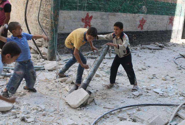 Các cậu bé dựng ống thép giả vờ làm súng phóng đạn cối tại hiện trường bị ném bom bởi quân đội chính phủ ở thành phố Aleppo, Syria.