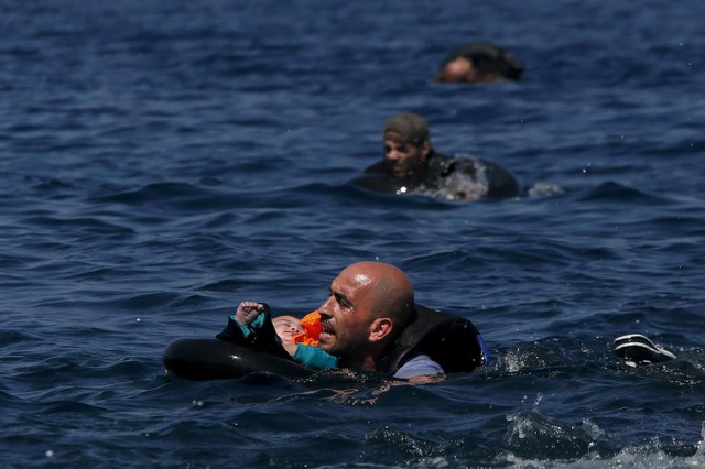 
Người đàn ông Syria ôm con nhỏ nằm trên phao trong khi cố gắng bơi vào bờ sau khi thuyền của họ bị xì hơi gần đảo Lesbos, Hi Lạp.
