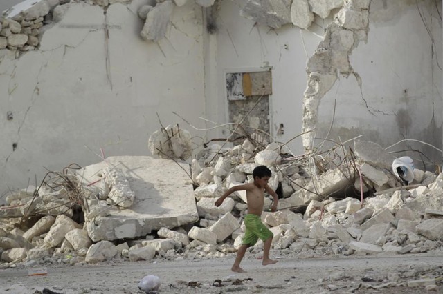 Cậu bé đi chân trần qua những ngôi nhà bị phá hủy bởi nội chiến tại thành phố Maaret al-Numan, Syria.