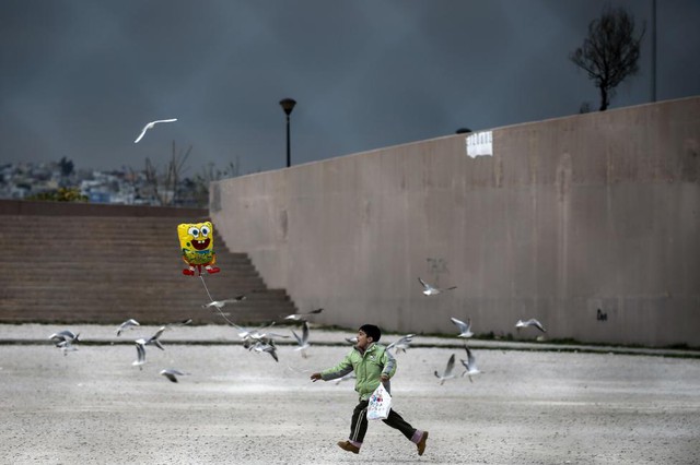 Cậu bé di cư chơi với bóng bay bên ngoài sân vận động Tae Kwon Do ở ngoại ô thành phố Athens, Hi Lạp.