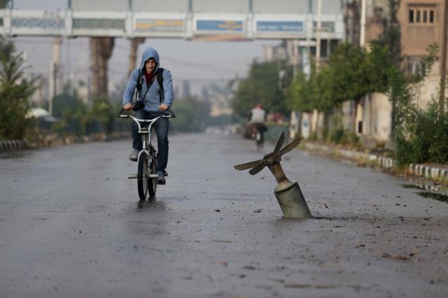 Một người dân địa phương đạp xe ngang một phần quả bom đã phát nổ tại thị trấn Douma, phía đông Ghouta ở Damascus, Syria ngày 5-11