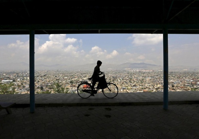 Cậu bé đạp xe trên đỉnh đồi nhìn xuống thành phố Kabul, Afghanistan.