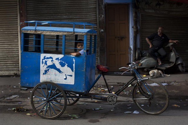 Cậu bé ngồi chờ trên xe ba bánh trên đường tới trường ở thành phố New Delhi, Ấn Độ.