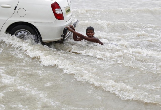 Cậu bé bám phía sau một chiếc xe taxi đang di chuyển trên đường phố ngập lụt ở Allahabad, Ấn Độ.