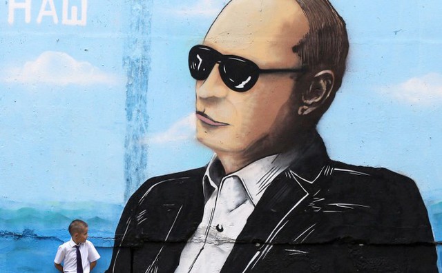 Cậu bé đứng cạnh bức tranh graffiti vẽ chân dung Tổng thống Nga Vladimir Putin tại thành phố Simferopol, Crimea.