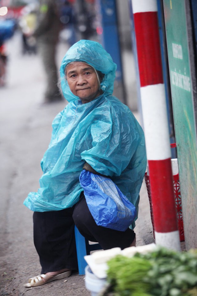 Cụ già bán rau trên đường Tôn Đức Thắng mặc áo mưa mỏng để chống lại cái lạnh ùa về trên phố.
