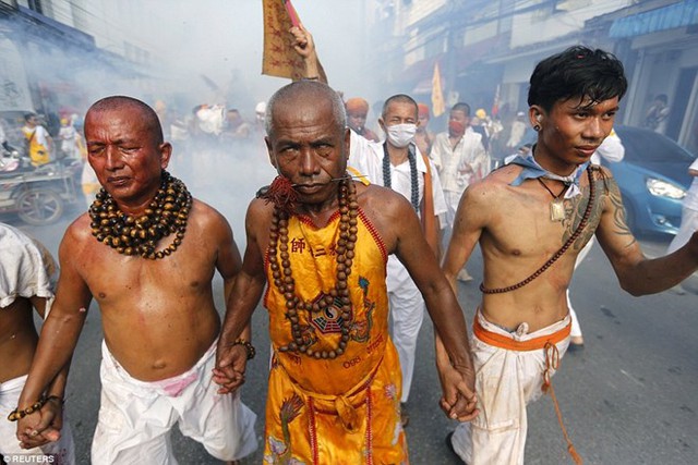 Ba tín đồ, trong đó có một người có vẻ như đang dính rất nhiều máu ở vùng bụng, nắm tay nhau khi diễu hành qua đường phố. (Nguồn: Reuters)