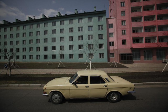 Chiếc xe hơi đi qua hai chung cư mới xây được sơn màu xanh và đỏ ở Bình Nhưỡng.