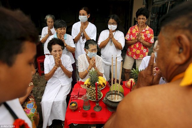 Bảy người phụ nữ, trong đó có nhiều người đeo khẩu trang, ngồi bên vệ đường và tỏ thái độ tôn trọng và kính cẩn khi những người đàn ông rước đám qua chỗ họ. (Nguồn: Reuters)