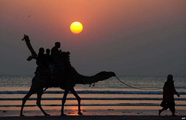 Du khách cưỡi lạc đà đi trên bãi biển Clifton ở Karachi, Pakistan.