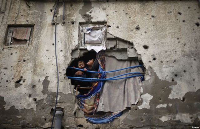 Trẻ em người Palestine nhìn qua lỗ thủng trên tường nhà của họ ở thành phố Gaza. Các nhân chứng cho biết ngôi nhà bị tàn phá trong cuộc không kích của quân đội Israel vào năm ngoái.