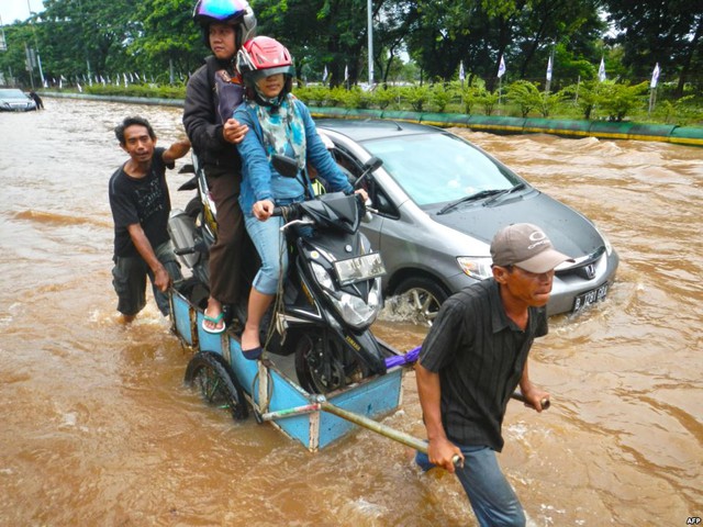 Hai người đàn ông kéo xe chở người đi xe máy qua đoạn đường ngập lụt ở Jakarta. Mưa lớn trong nhiều ngày đã khiến nhiều đoạn đường ở thủ đô của Indonesia ngập trong nước.
