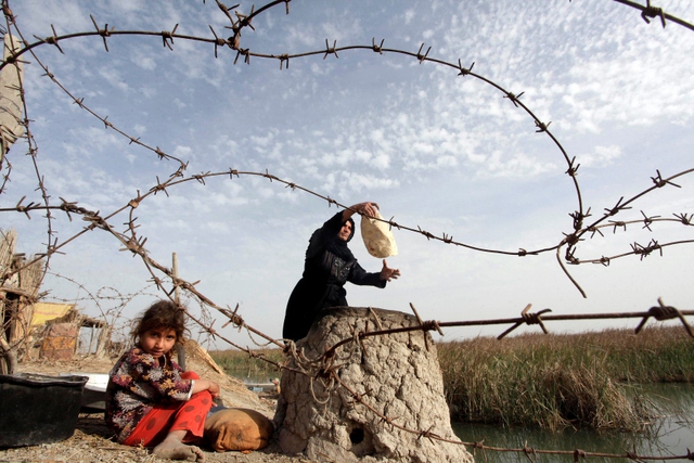 Bé gái ngồi cạnh người phụ nữ đang nướng bánh mì ở Baghdad, Iraq.