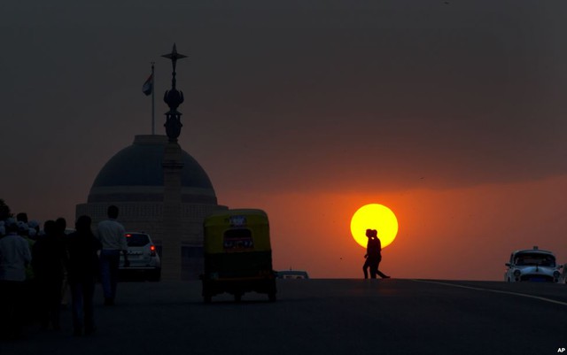 Mọi người trở về nhà sau giờ làm việc khi mặt trời đang lặn sau Dinh tổng thống trên đồi Raisina ở New Delhi, Ấn Độ.