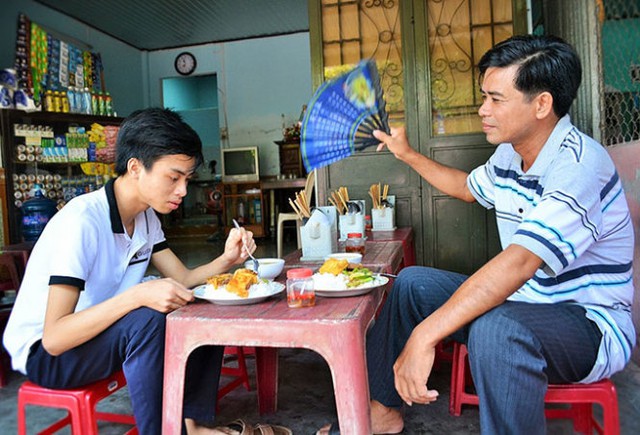 Ông Lê Đình Tuấn quạt mát cho con trong bữa ăn trưa. Ảnh được chụp trong những ngày thi cử nắng nóng ở Huế (nguồn ảnh: Tuổi trẻ)