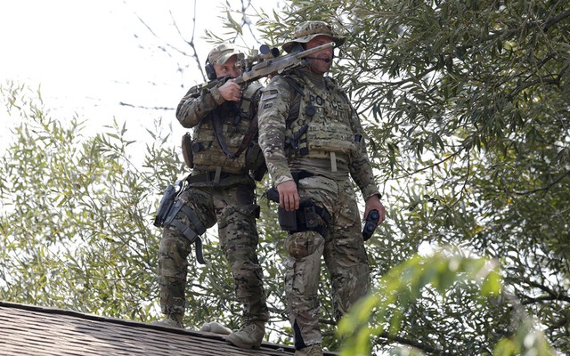 Lính bắn tỉa đứng trên mái nhà trong cuộc truy tìm hai nghi phạm giết hại một cảnh sát ở Fox Lake, bang Illinois, Mỹ.