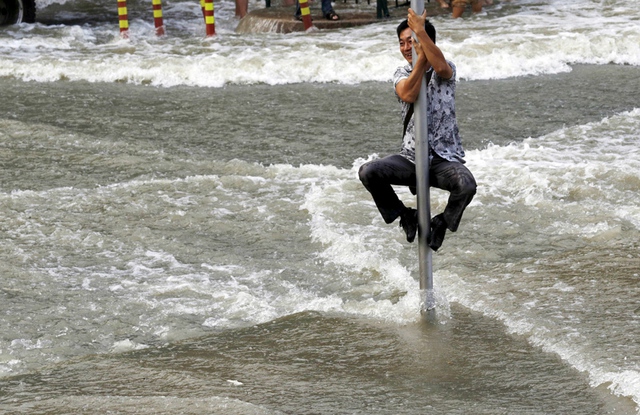 Người đàn ông trèo lên cột biển báo giao thông để tránh sóng thủy triều đánh vào bờ từ sông Tiền Đường ở thành phố Hàng Châu, Trung Quốc.