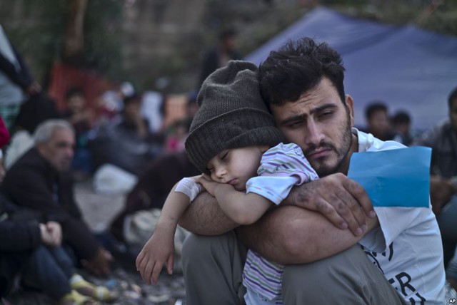 
Em bé di cư người Syria ngủ trong vòng tay bố trong khi chờ xe bus tại một điểm tập trung trên đảo Lesbos, Hi Lạp.
