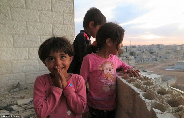 
Ba đứa trẻ nhìn thành phố bị chiến tranh tàn phá từ một tòa nhà cao tầng.
