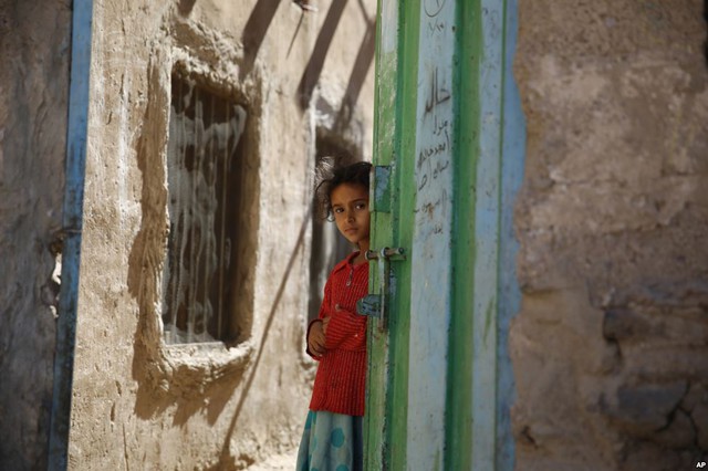 Bé gái đứng trước cửa trong khi nhìn những đứa trẻ khác được tiêm vắc-xin phòng bại liệt tại nhà ở thành phố Sanaa, Yemen.