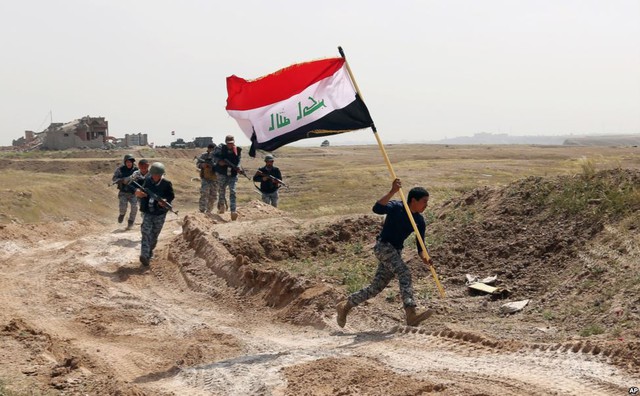 Thành viên của lực lượng an ninh Iraq chạy cắm cờ tại một cao điểm trong cuộc chiến chiếm lại thành phố Tikrit từ nhóm phiến quân Nhà nước Hồi giáo (IS).