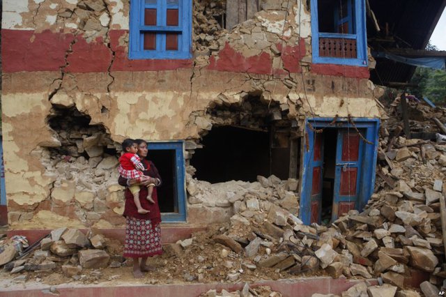 Người phụ nữ bế con đứng bên ngoài ngôi nhà bị phá hủy bởi động đất ở ngoại ô Lalitpur, Nepal.