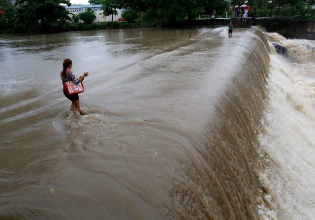 Người dân địa phương lội qua mặt đập tràn chìm trong nước trên sông ở Las Pinas, Philippines.